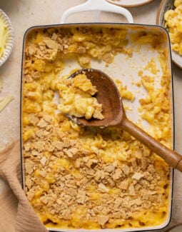 gluten free mac and cheese topped with crackers in a casserole dish with a serving spoon taking a scoop out