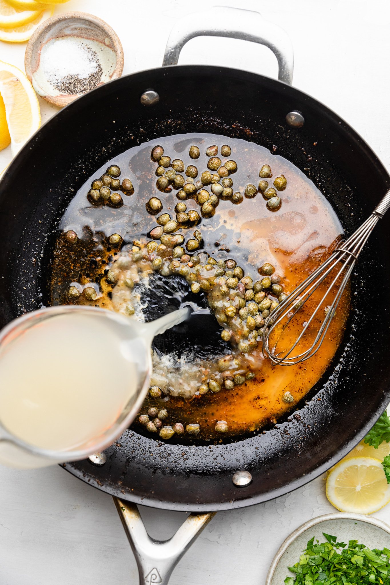 pouring broth into a skillet with lemon juice and capers