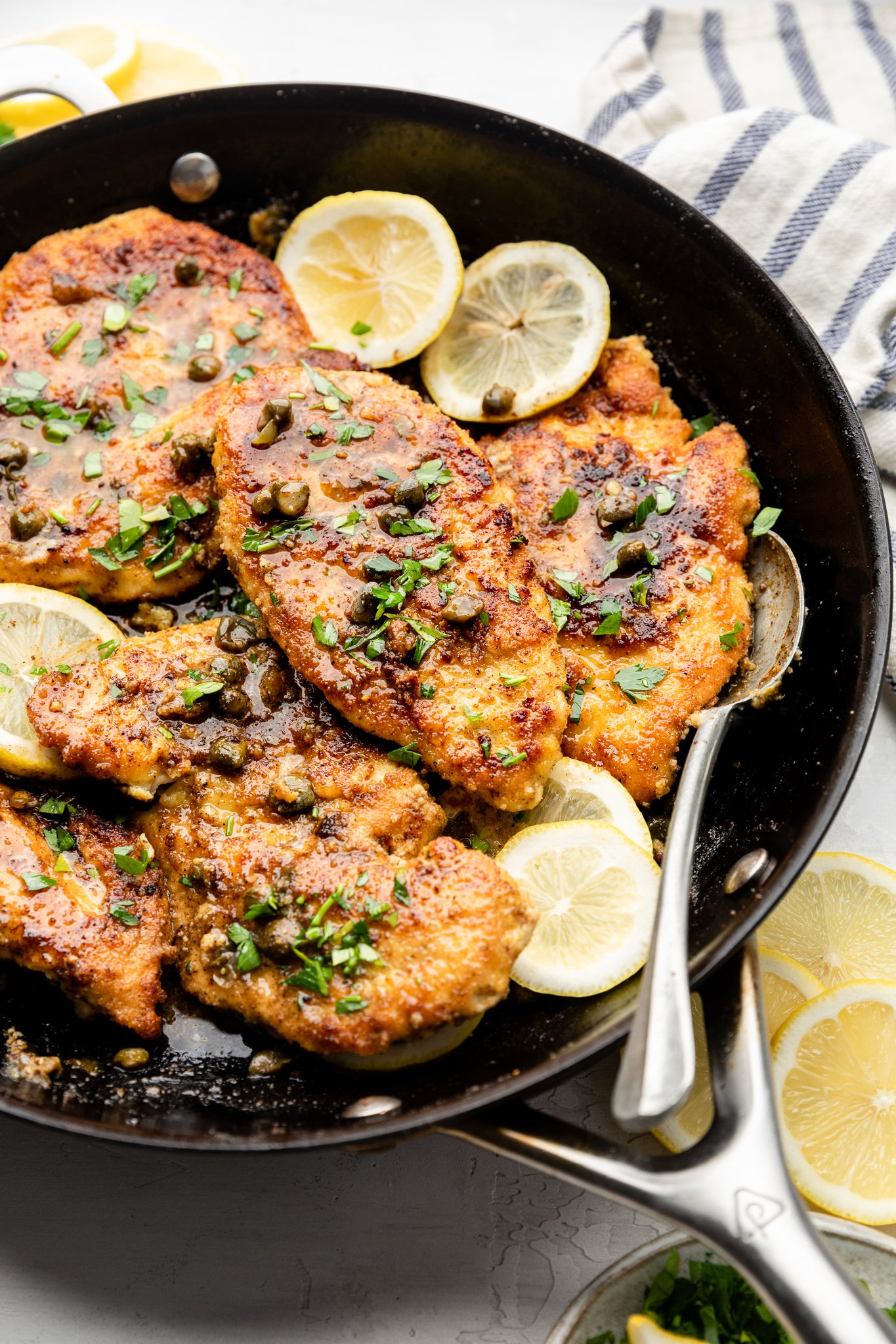 chicken piccata with capers and lemon slices in a skillet with a silver spoon