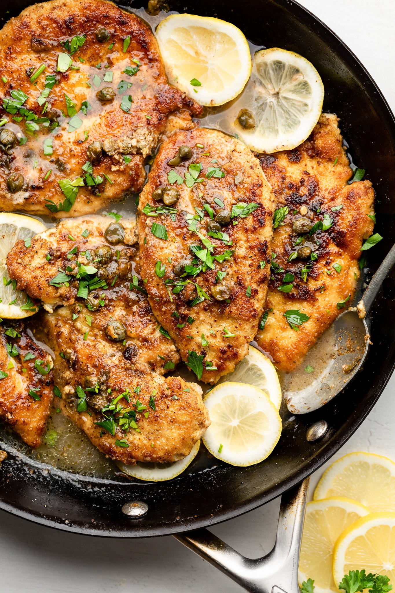 a skillet with gluten free chicken piccata, capers, lemon slices, and parsley