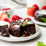 mini chocolate lava cake on a plate with mint leaves and raspberries and strawberries in the background