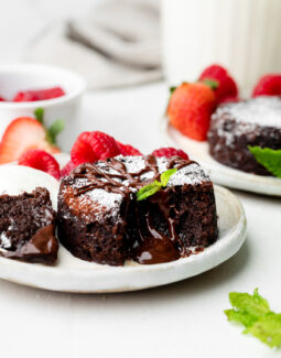mini chocolate lava cake on a plate with mint leaves and raspberries and strawberries in the background