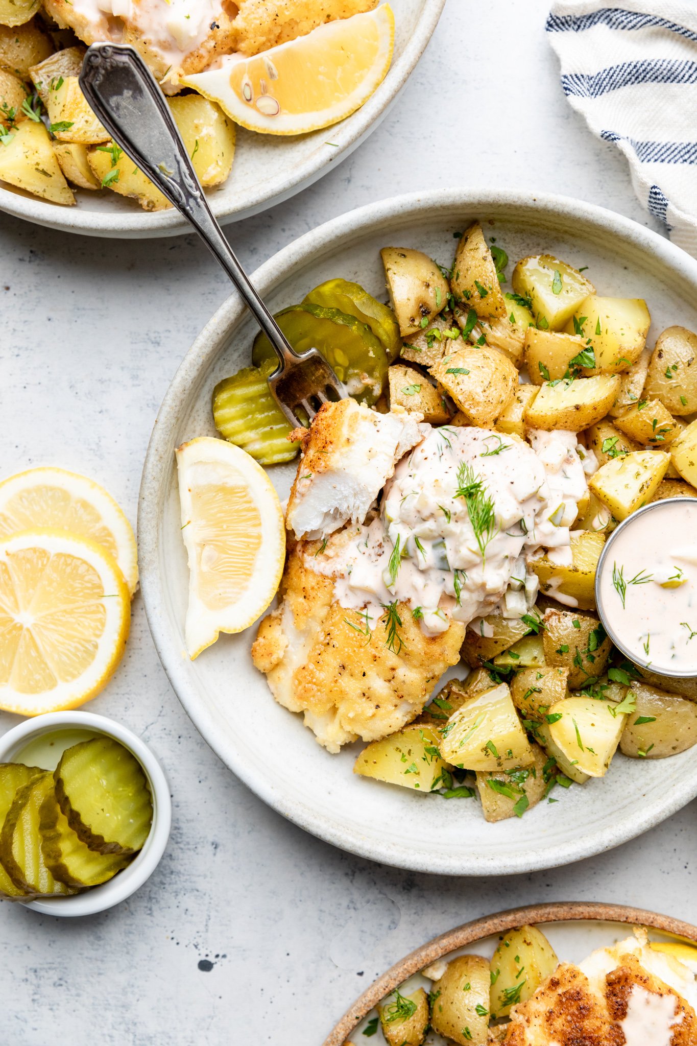 Gluten Free Fish and Chips with potatoes, tartar sauce, and lemon and pickles in a bowl