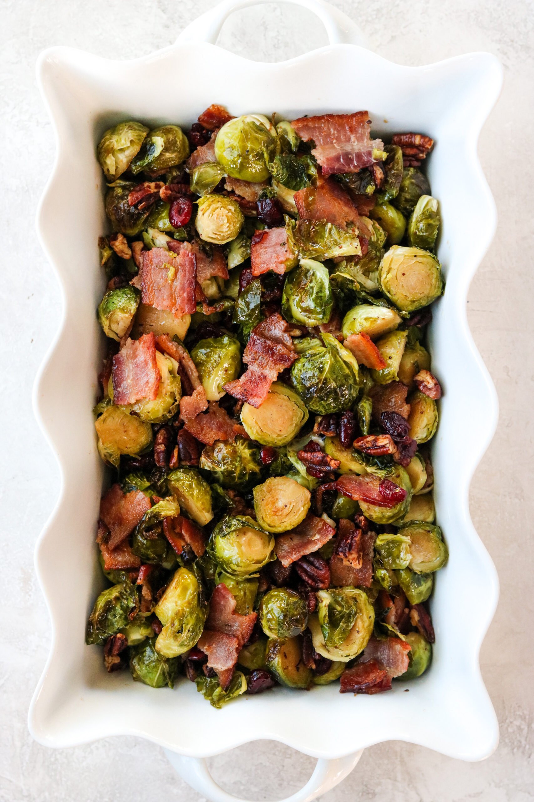 roasted brussel sprouts in a white casserole dish with bacon, dried cranberries, and pecans