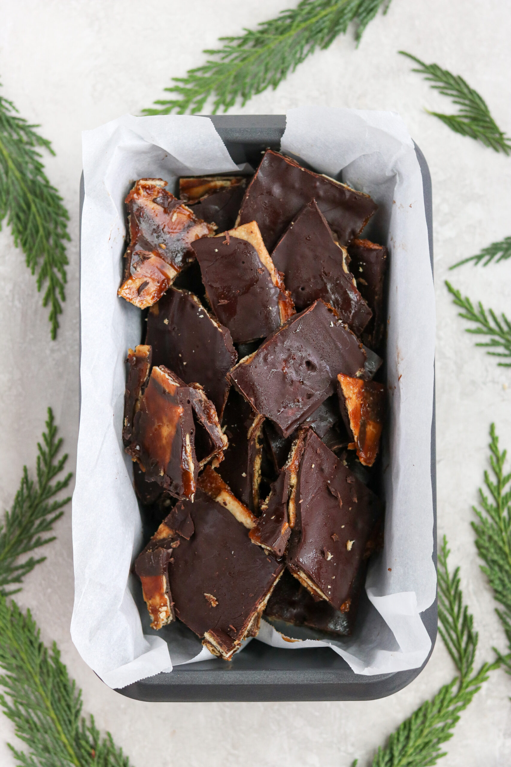 A loaf pan lined with parchment paper and filled with paleo Christmas crack with pine leaves 
