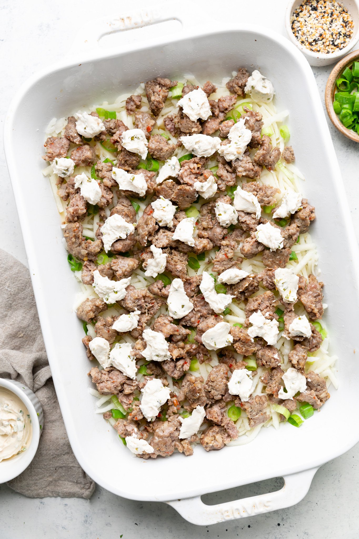 Sausage, dairy free cream cheese, green onions, and hash browns in a casserole dish