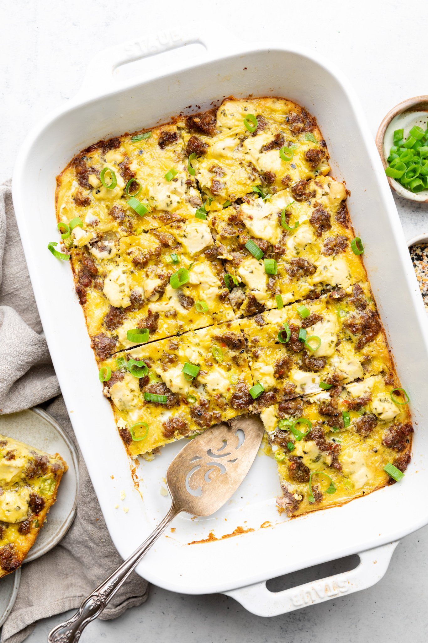 Sausage Hash brown casserole with green onions sliced in a white Staub casserole dish