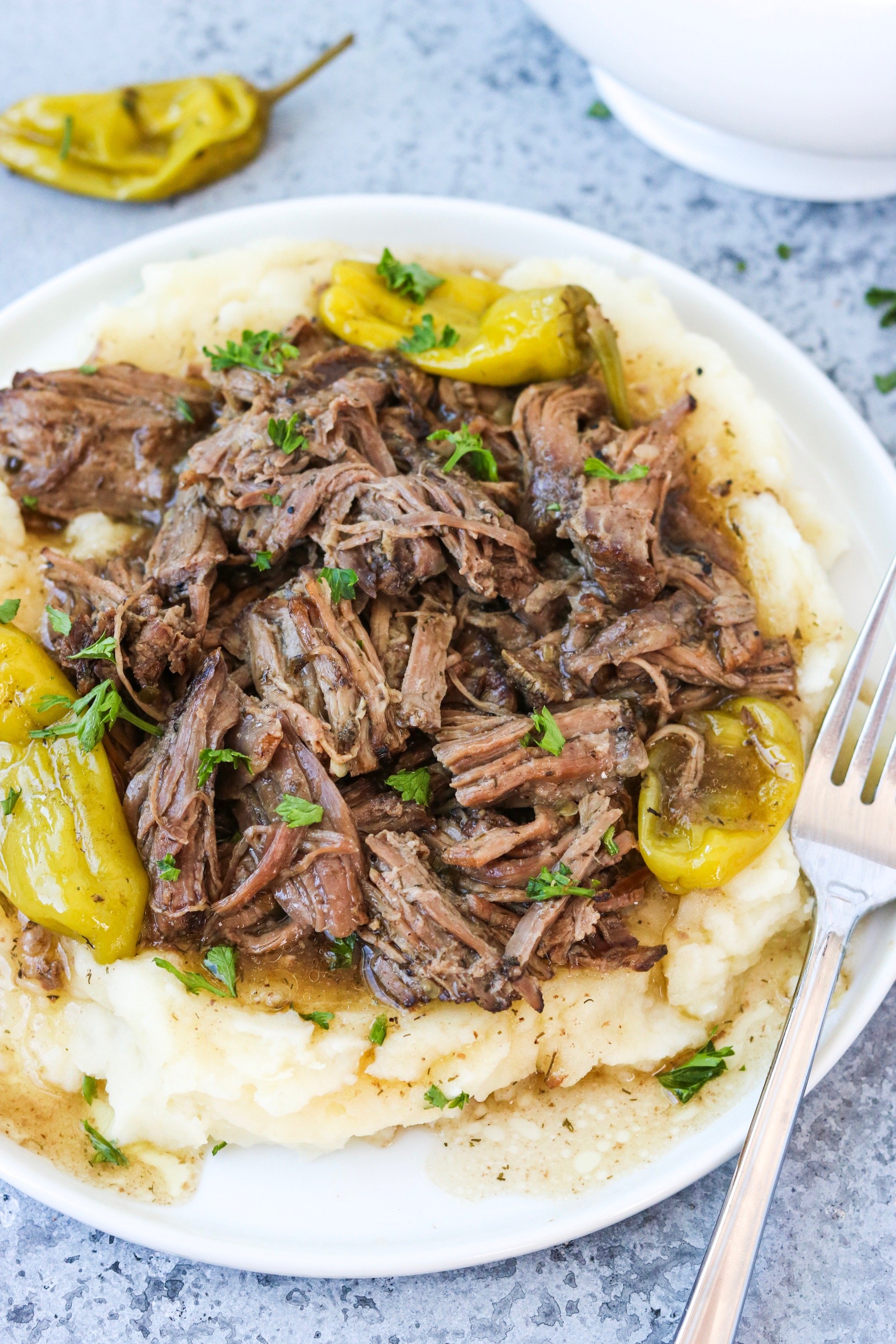 shredded beef with gravy and pepperoncinis over garlic cauliflower mash on a white plate
