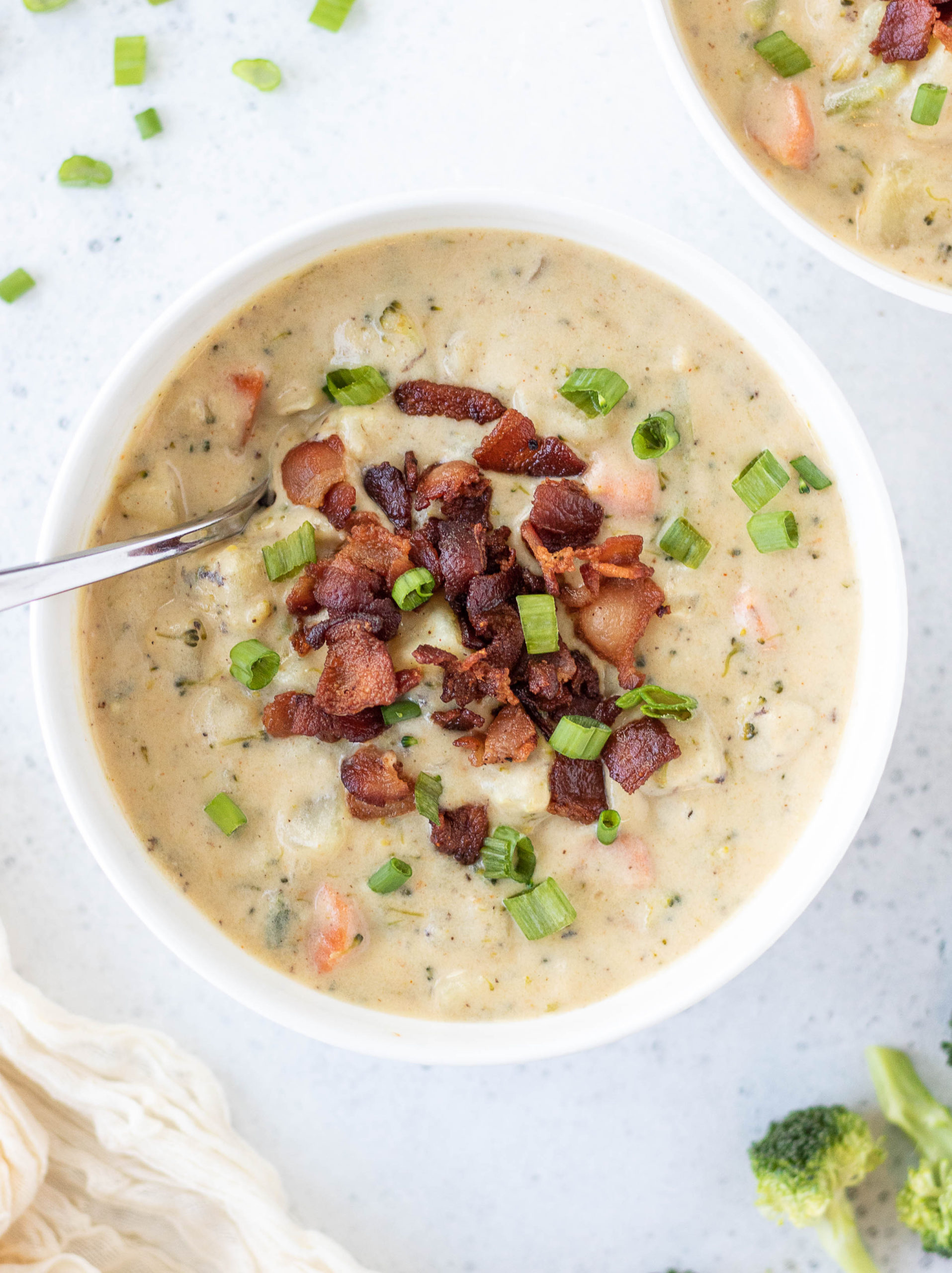a white bowl of potato soup with bacon and green onions with a silver spoon