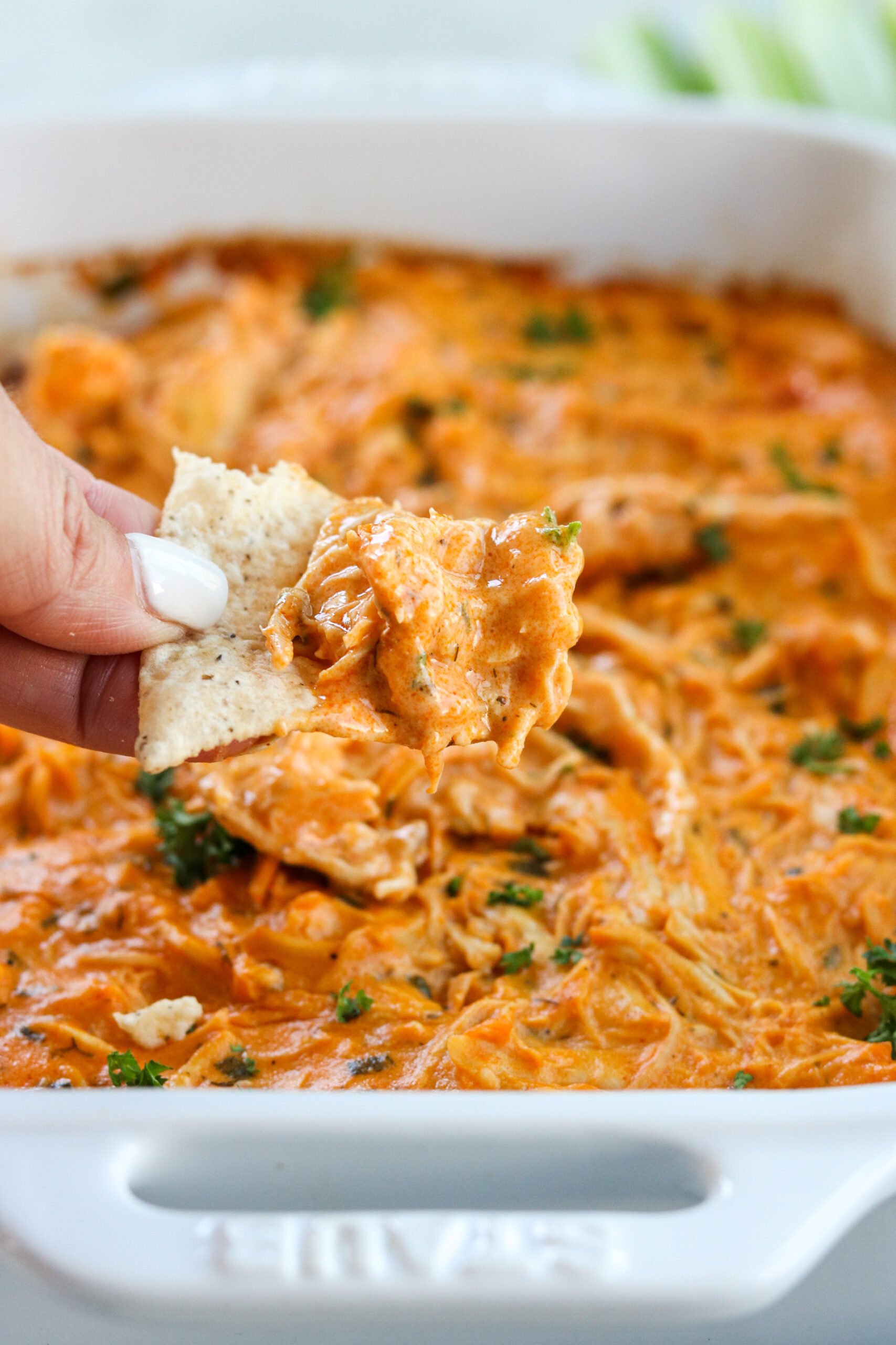A hand with a chip scooping up some buffalo chicken dip