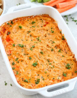 Healthy buffalo chicken dip in a white Staub baking dish topped with parsley with carrots and celery in the background