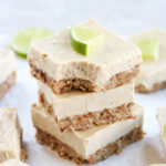 Vegan key lime cheesecake bars stacked on top of each other with a lime slice on top