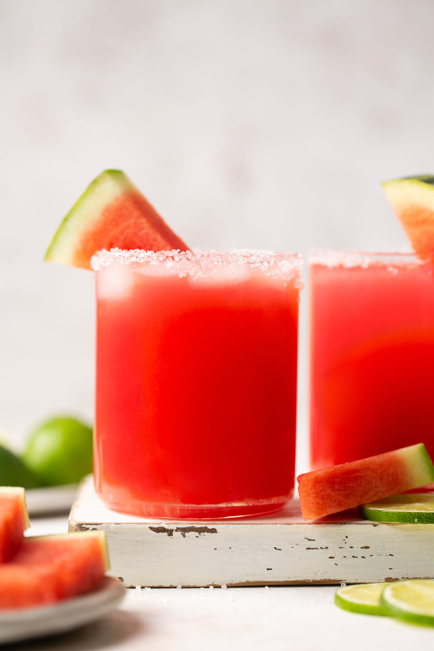 a watermelon margarita in a salt-rimmed glass on a white board with a slice of watermelon for garnish