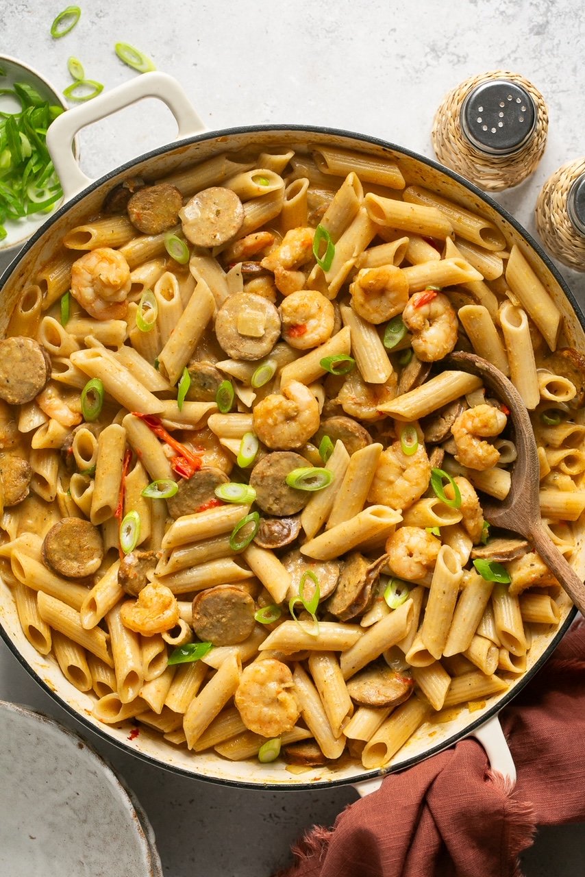 cajun shrimp and sausage pasta in a skillet topped with green onions