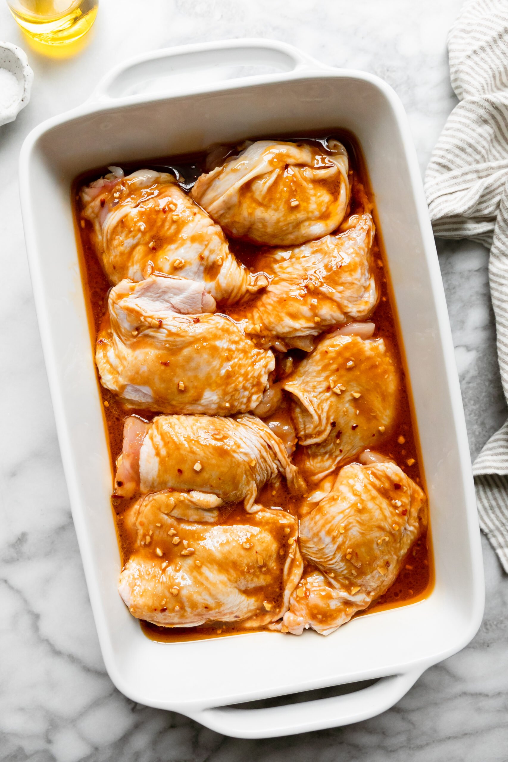 a white casserole dish filled with raw chicken thighs drenched in marinade
