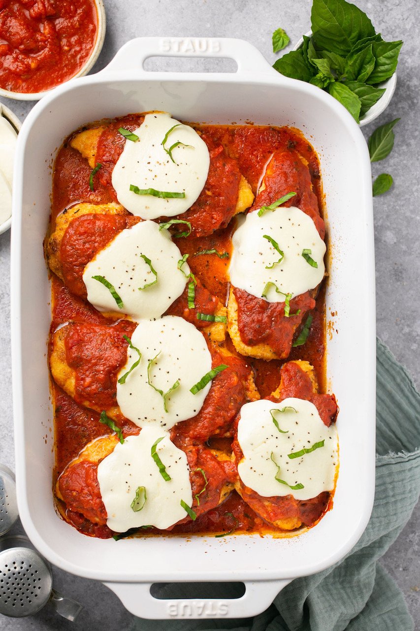 6 pieces of chicken parmesan in a white baking dish topped with basil