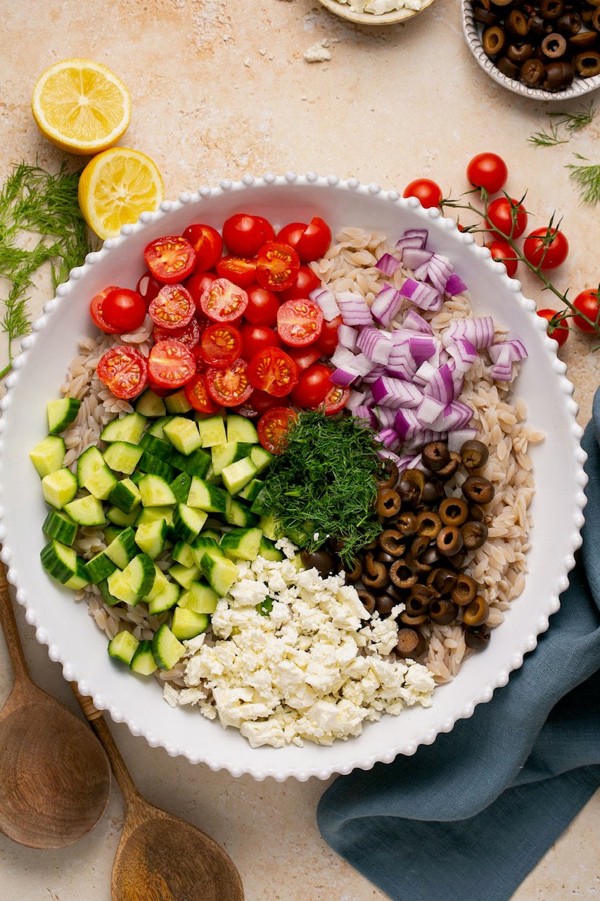 an overhead shot of the ingredients in gluten free orzo salad in a white bowl 