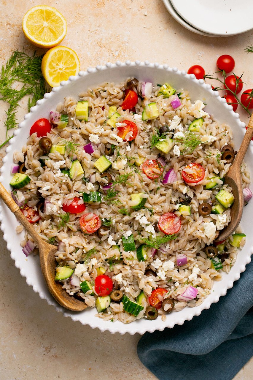 gluten free orzo Greek salad in a bowl with a wooden spoon
