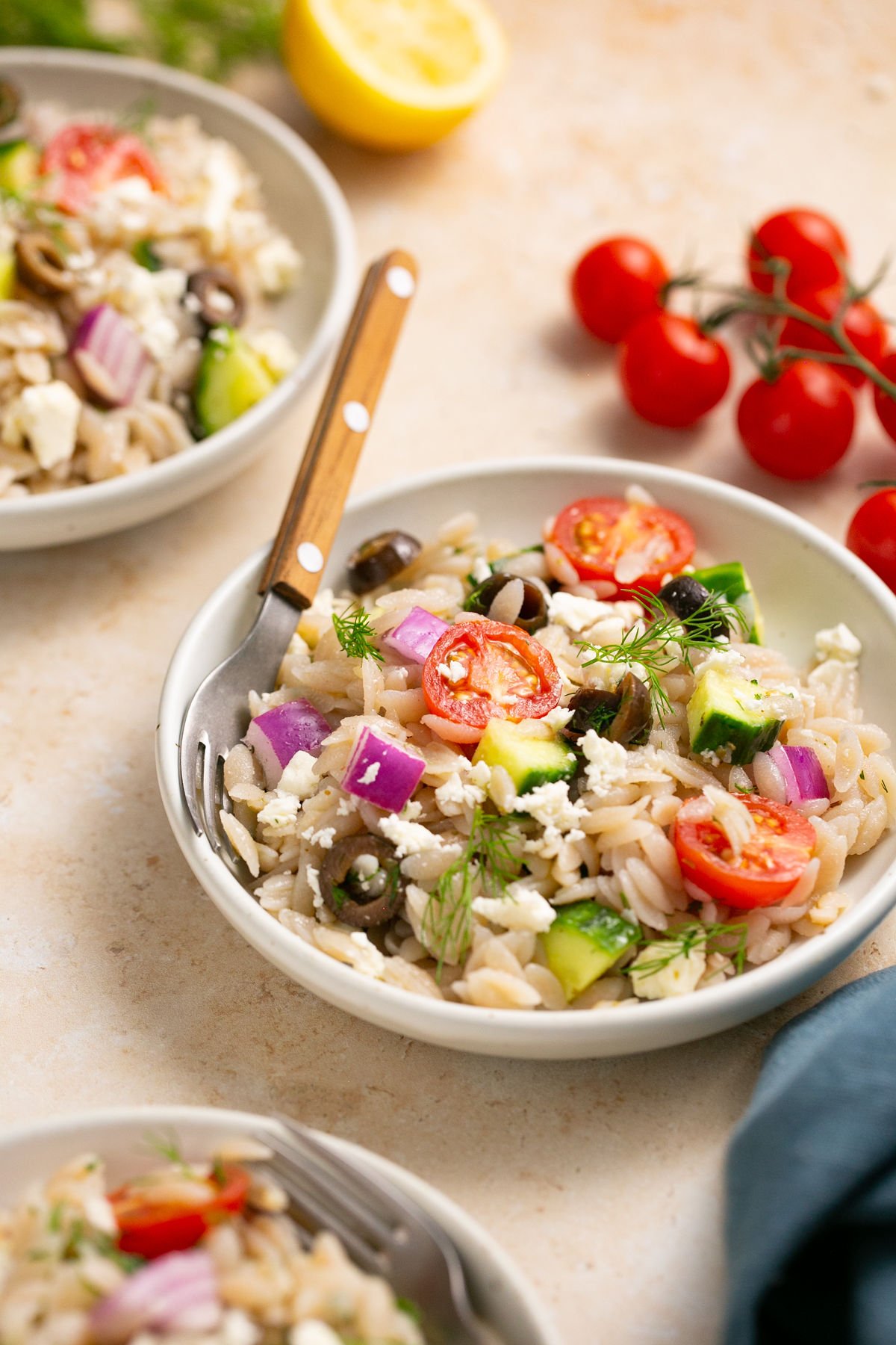 a small bowl filled with gluten free orzo and salad ingredients with a fork resting on the side. 