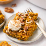 pumpkin baked oatmeal on a plate with a dollop of whipped cream and a gold fork