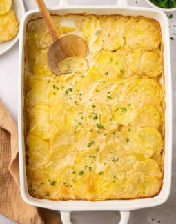 gluten free scalloped potatoes in a casserole dish with a wooden spoon taking a scoop out