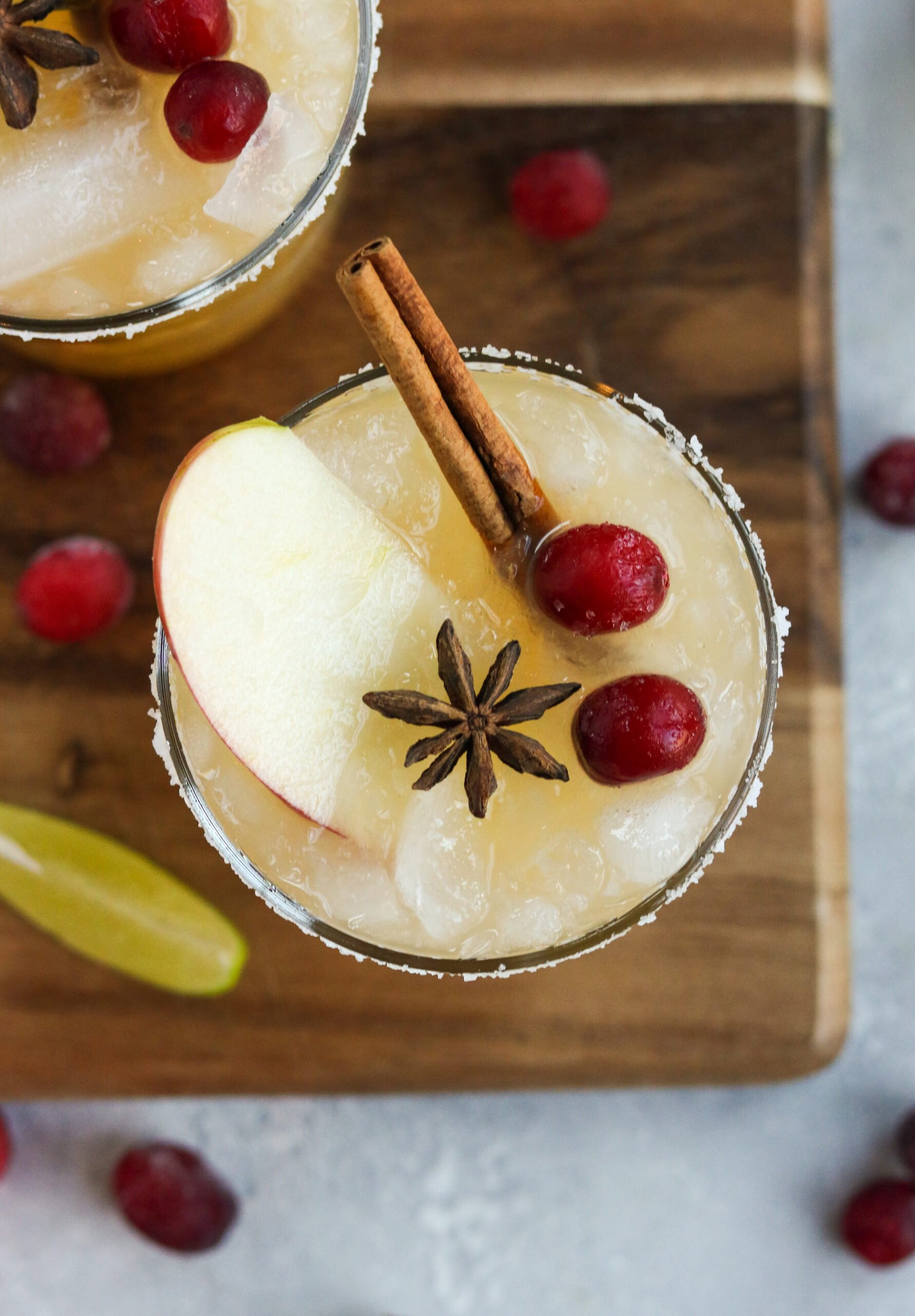thanksgiving margarita topped with a cinnamon stick, apple slice, and two cranberries