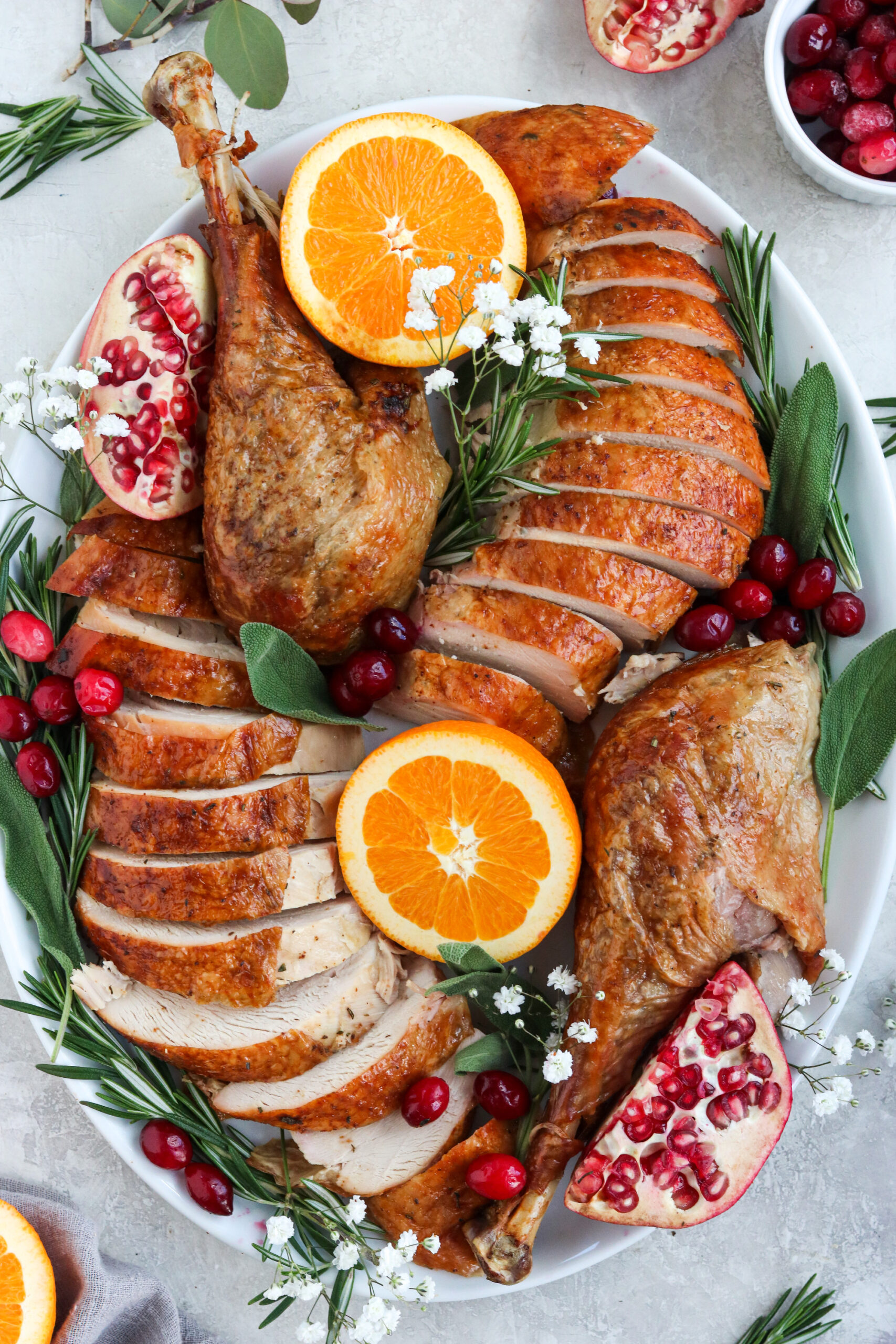 roasted turkey sliced up on a platter with pomegranates and oranges