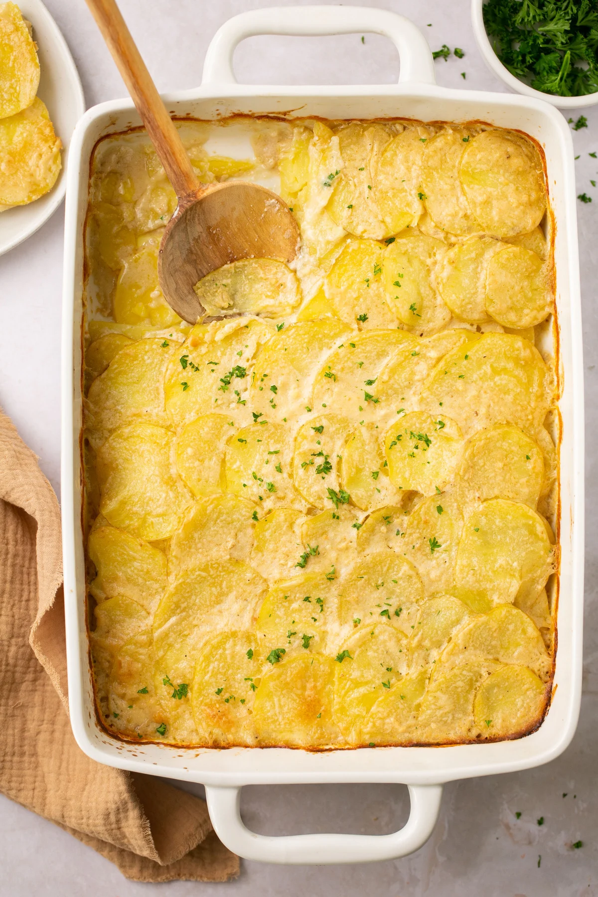 gluten free scalloped potatoes in a white casserole dish with a wooden spoon