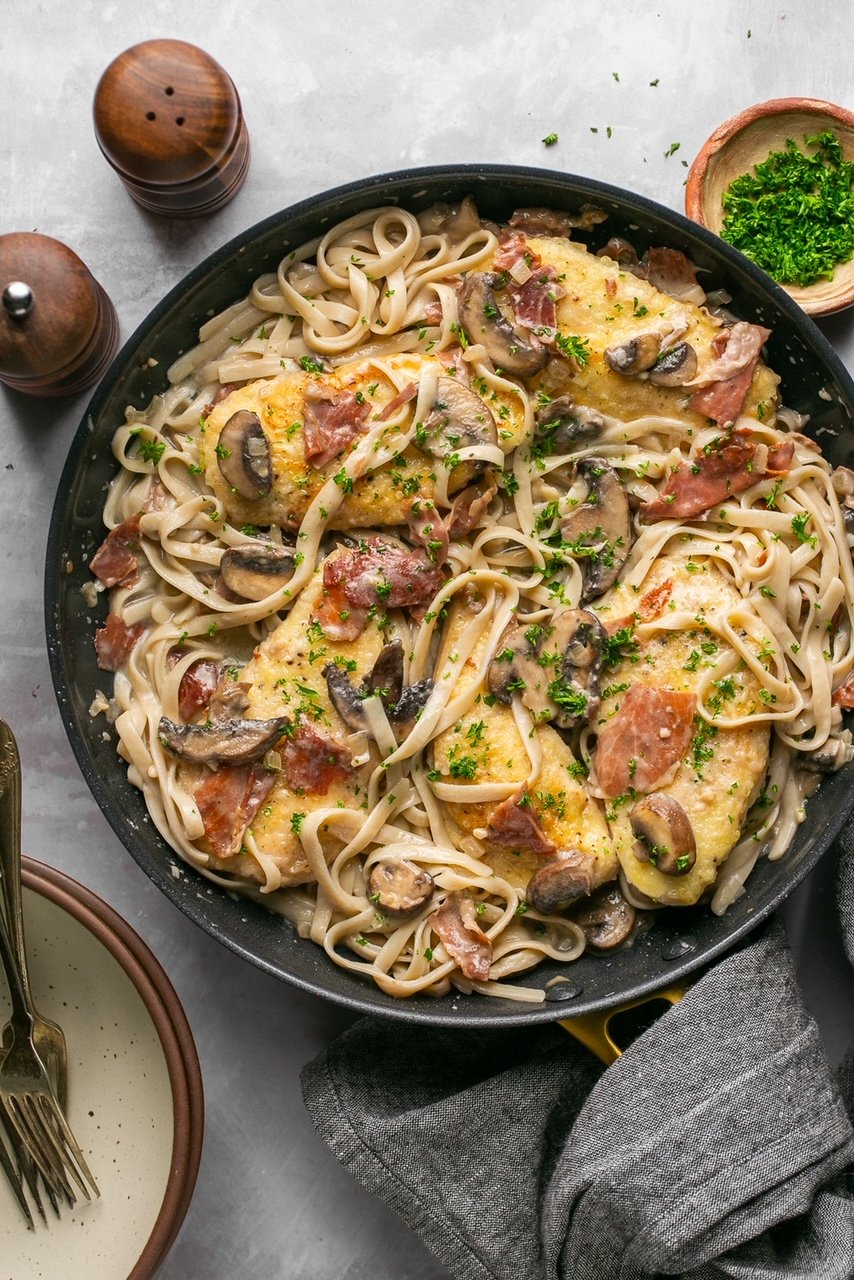 a skillet with fettucine and chicken marsala topped with parsley