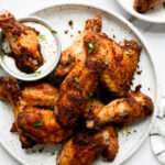 dry rubbed baked chicken wings on a white plate with one being dipped in ranch dressing