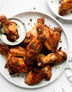 dry rubbed baked chicken wings on a white plate with one being dipped in ranch dressing