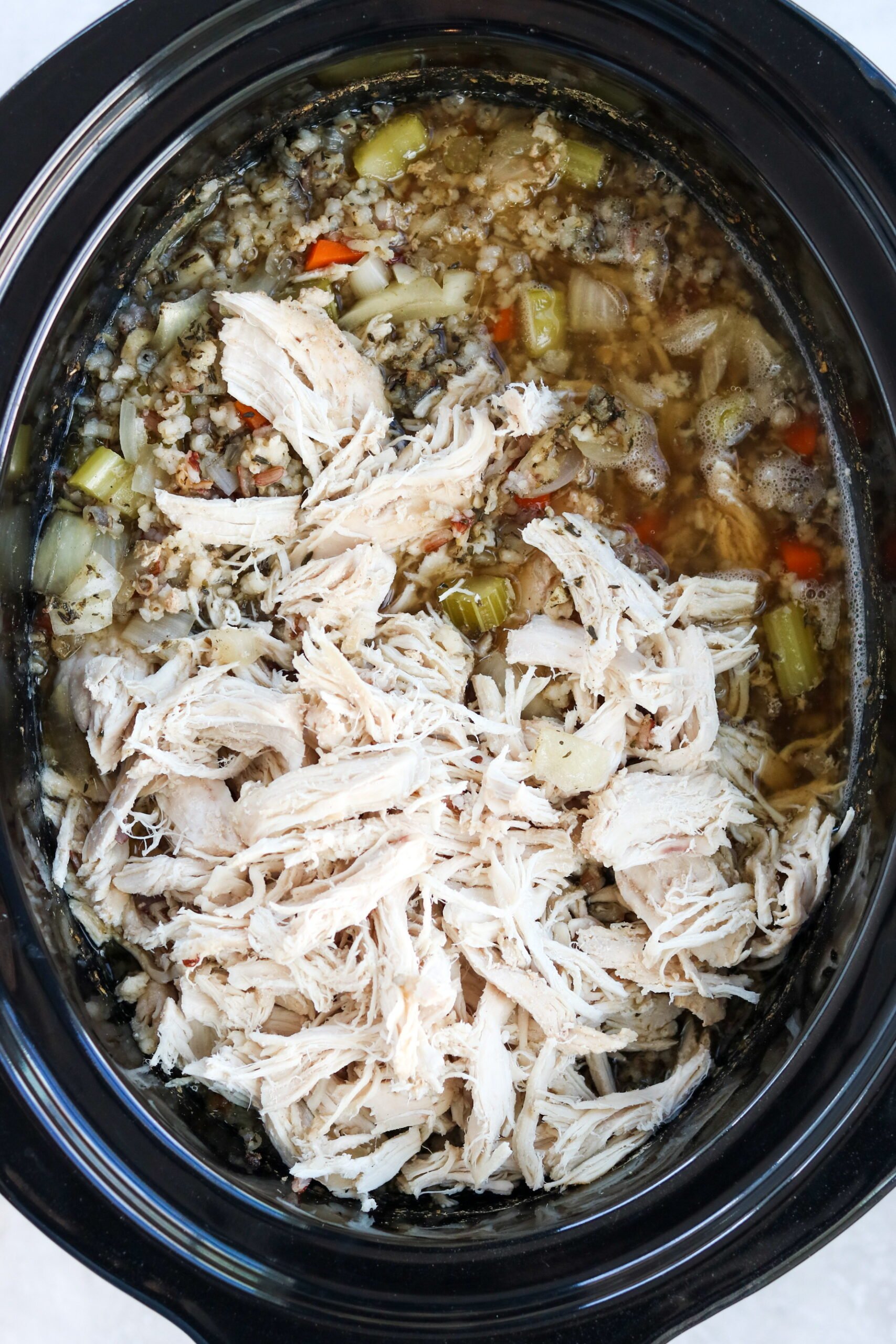 Shredded chicken on top of broth and vegetables in the slow cooker