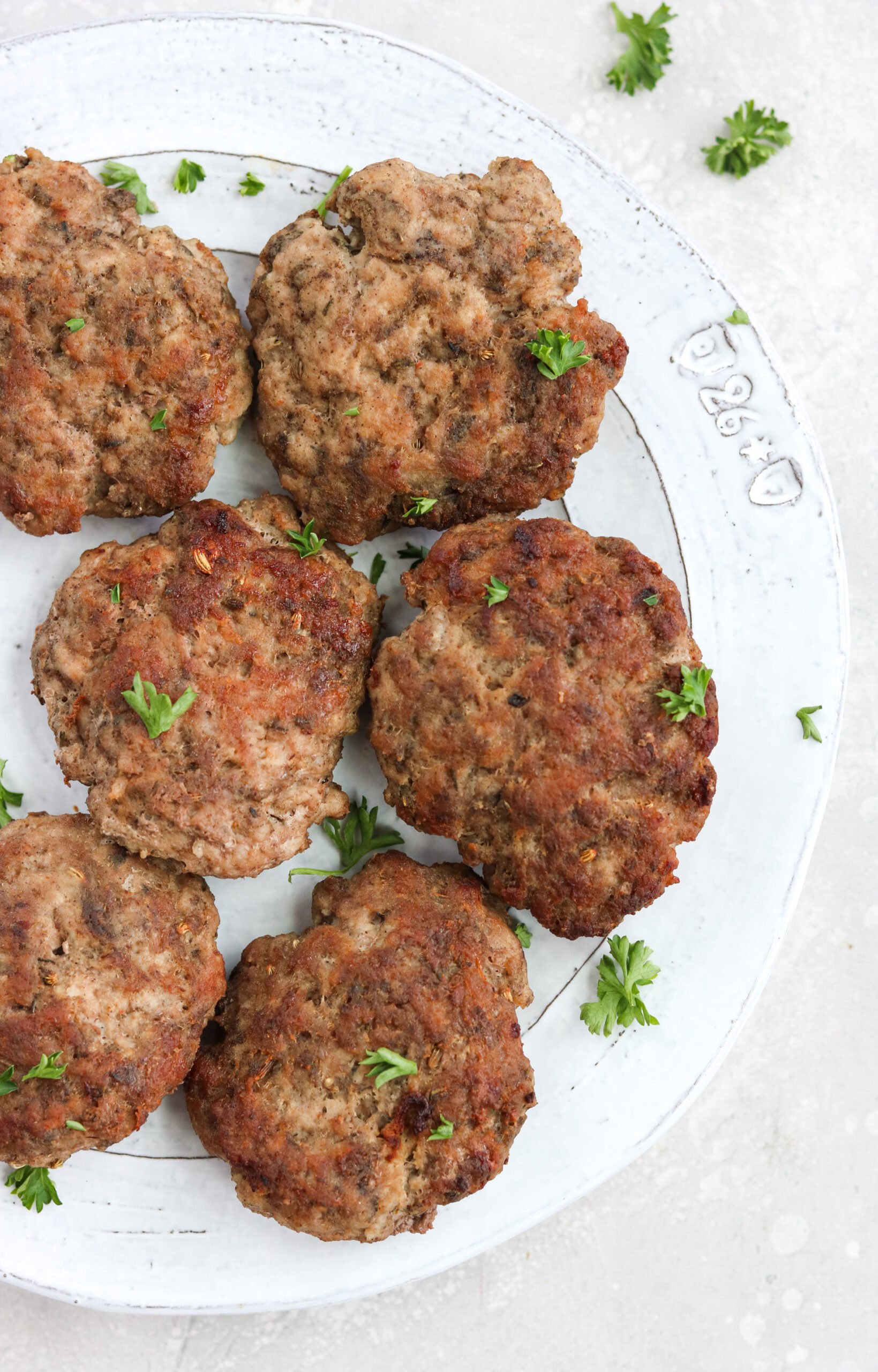 Air fryer sausage patties on a white plate topped with parsley
