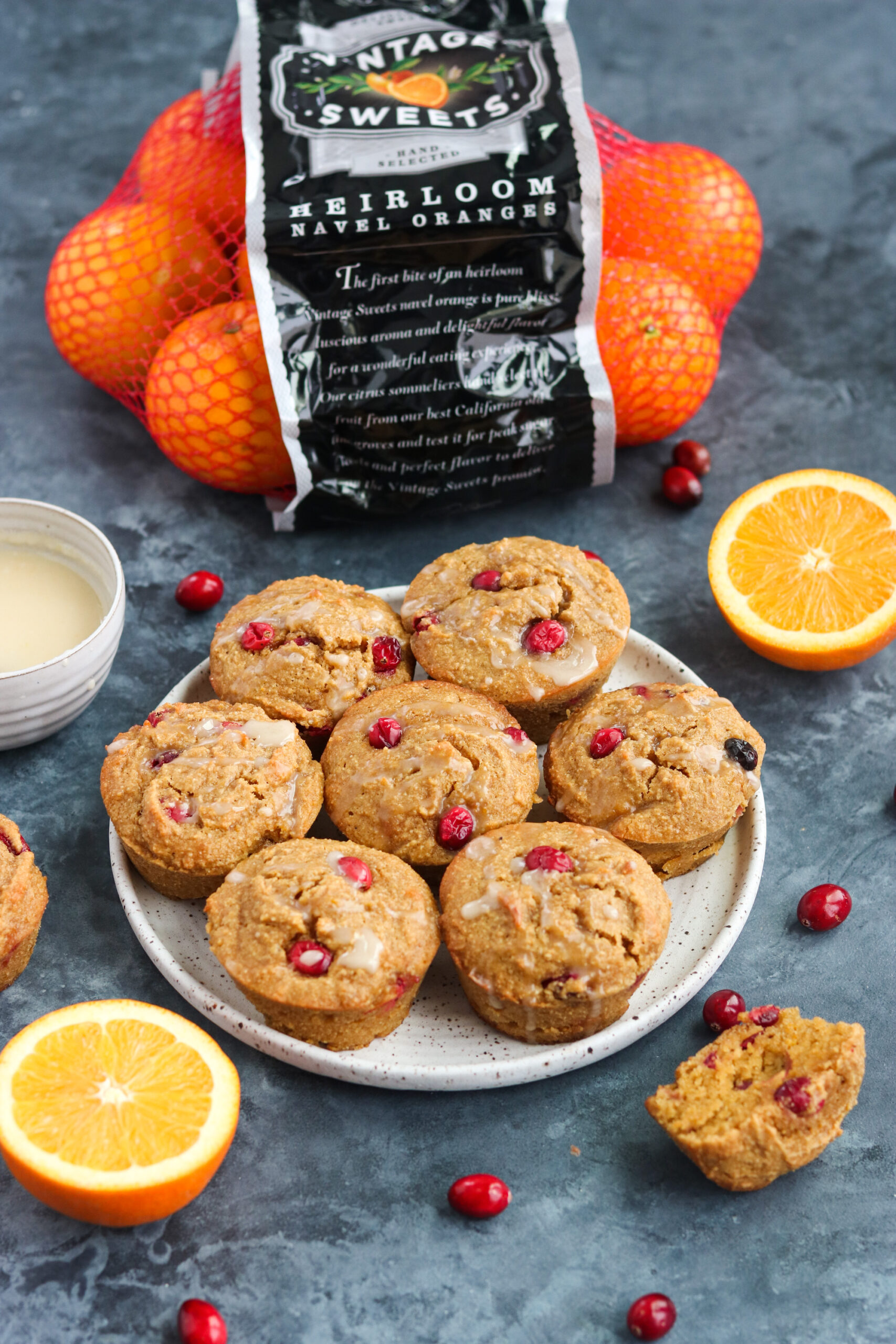 oranges surrounding cranberry orange muffins  on a plate