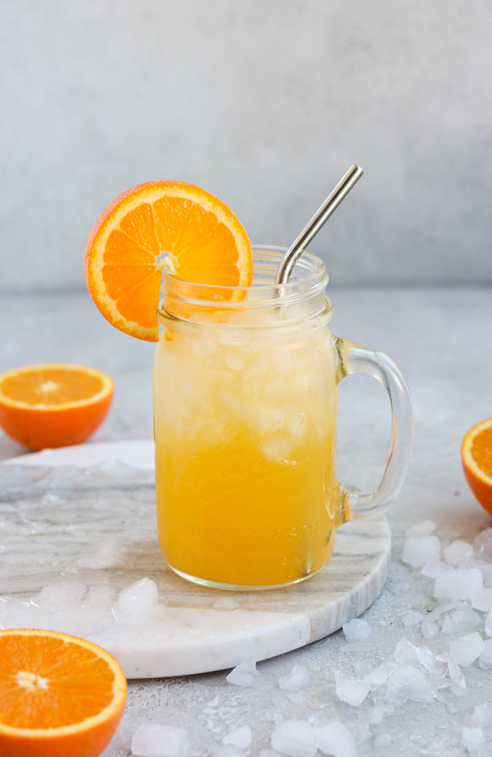 a glass of orange cocktail surrounded by ice and sliced oranges
