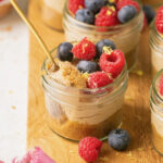 no bake mini cheesecakes in glass jars topped with berries with a spoon taking a bite