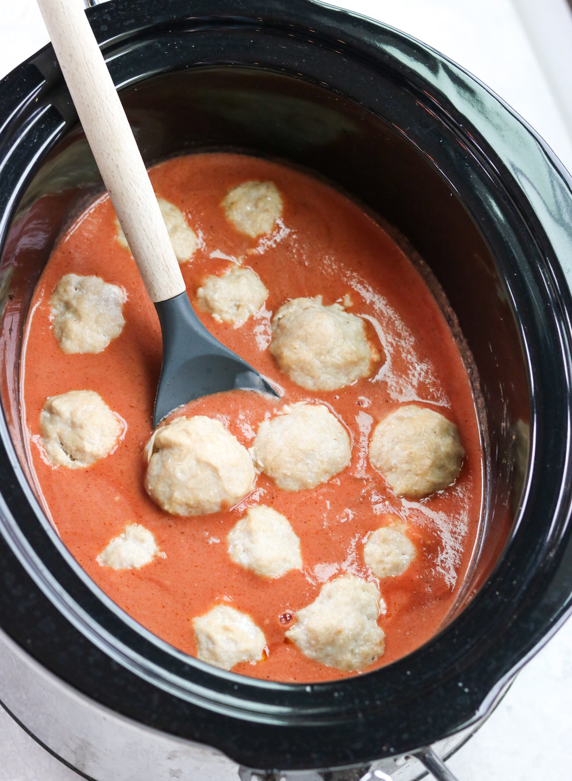 healthy chicken meatballs with creamy tomato curry sauce in a black slow cooker