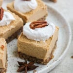 Paleo Vegan Pumpkin Cheesecake square with whipped cream and a pecan on a plate