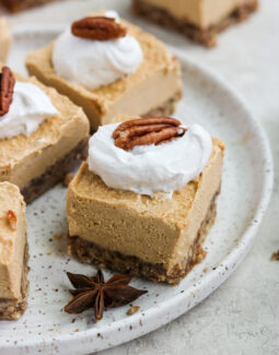 Paleo Vegan Pumpkin Cheesecake square with whipped cream and a pecan on a plate
