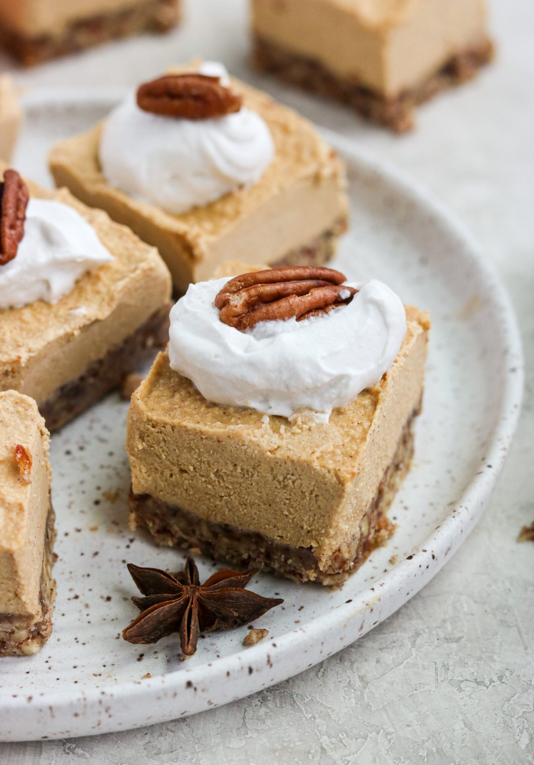 closeup of one bar with a pecan crust layered with pumpkin cheesecake and topped with whipped cream and a raw whole pecan.