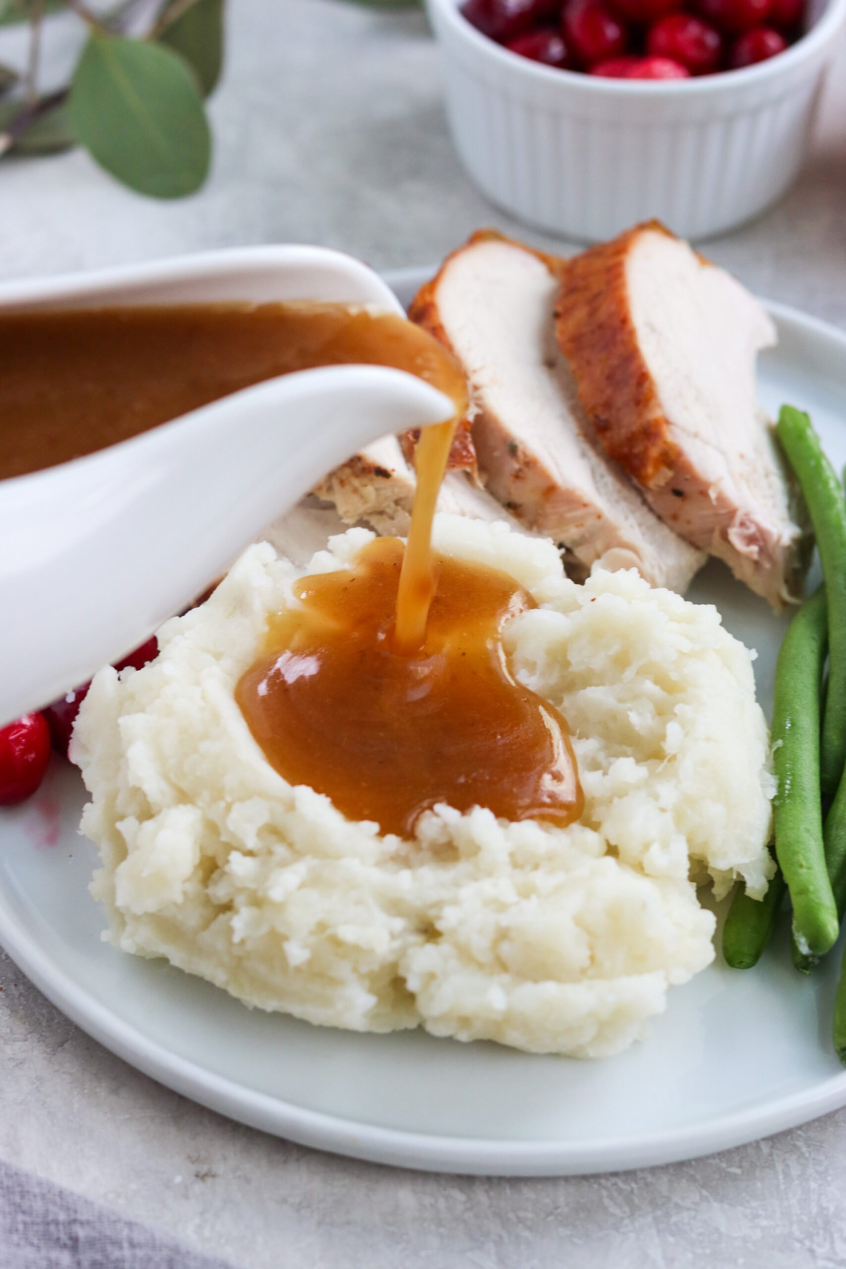 a white gravy dish full of gluten free graving pouring onto the top of mashed potatoes