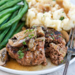 Salisbury steak with mashed potatoes and green beans on a white plate