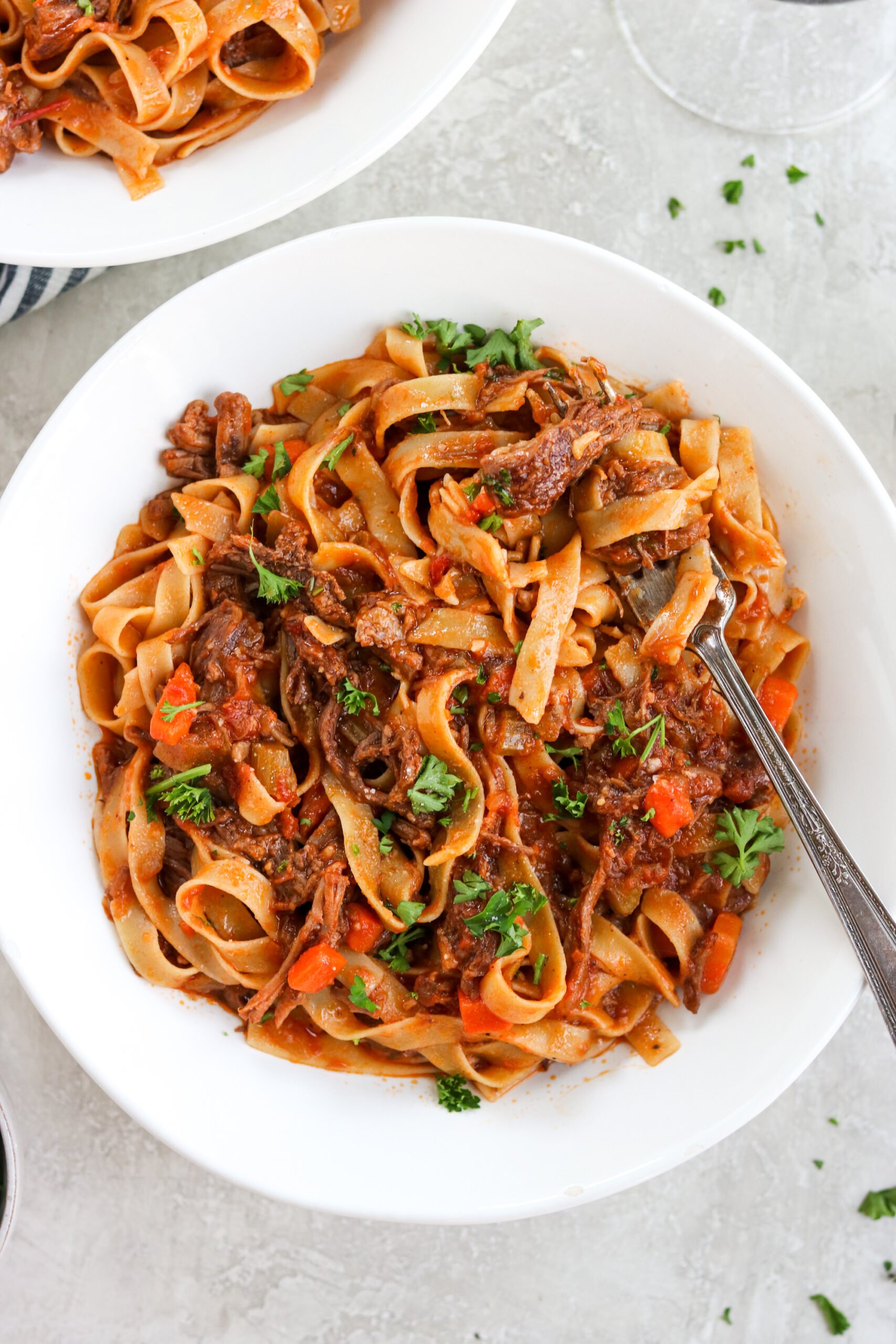 Beef ragu with a fork in a white bowl with parsley