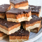 Vegan gluten free millionaire shortbread bars stacked on a plate. One has a bite out of it