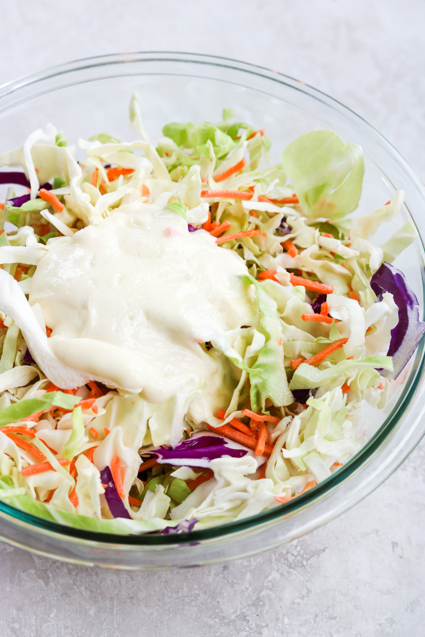 shredded cabbage, carrots, and mayo in a clear glass bowl