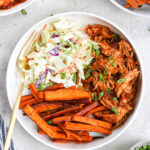 BBQ Chicken bowls with coleslaw and sweet potato fries topped with green onions in a white bowl