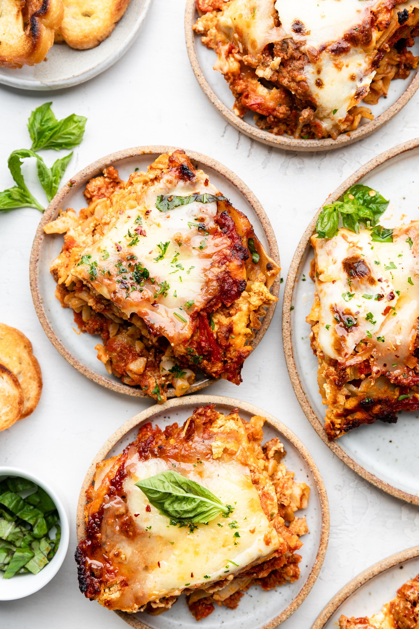 slices of gluten free lasagna on 4 different plates with basil