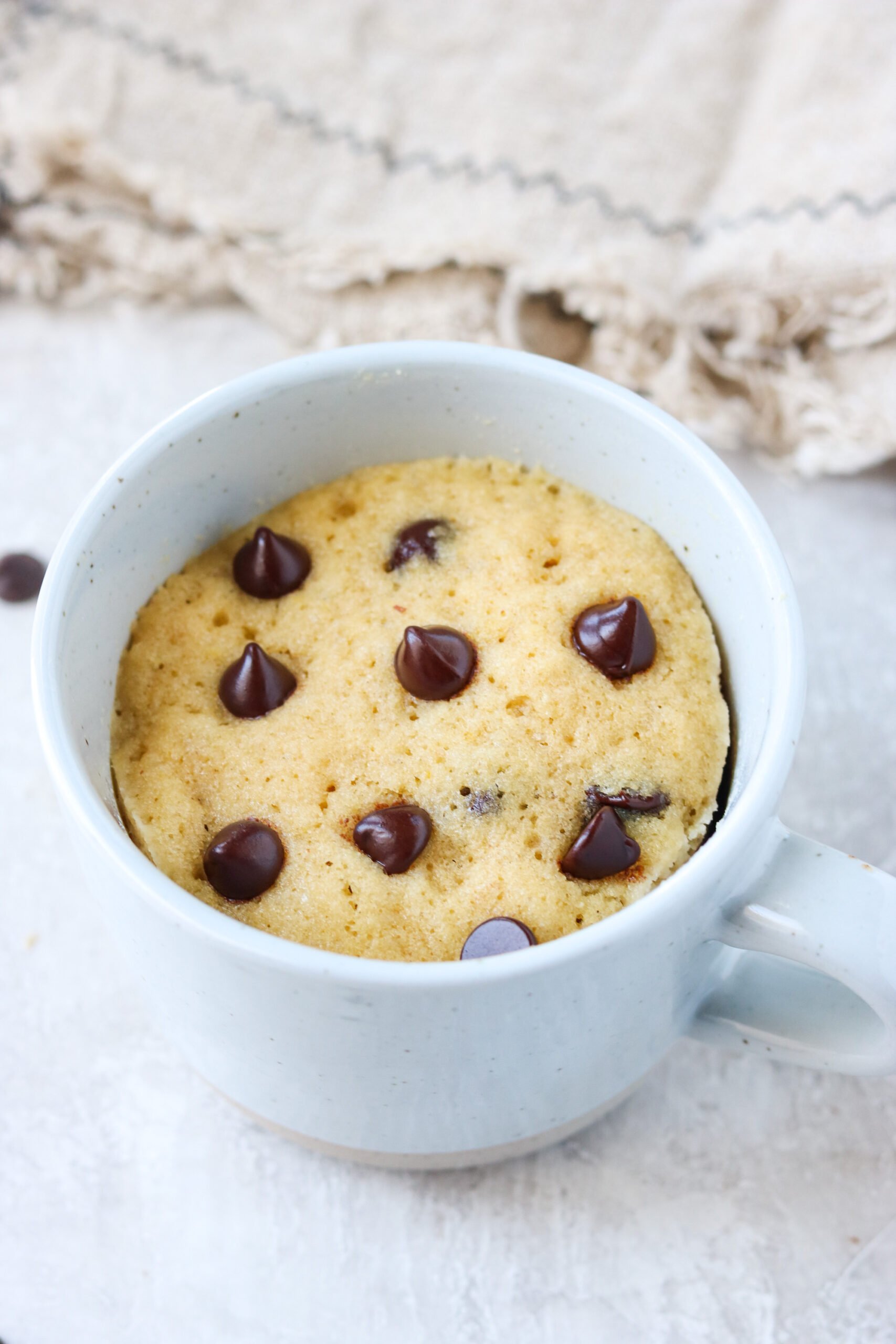 a close up of a white mug with cooked chocolate chip cake batter inside