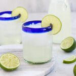 Homemade Lime Juice (Limeade) in a cup with a lime slice for garnish with another cup and a carafe the background surrounded by limes