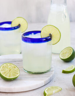 Homemade Lime Juice (Limeade) in a cup with a lime slice for garnish with another cup and a carafe the background surrounded by limes